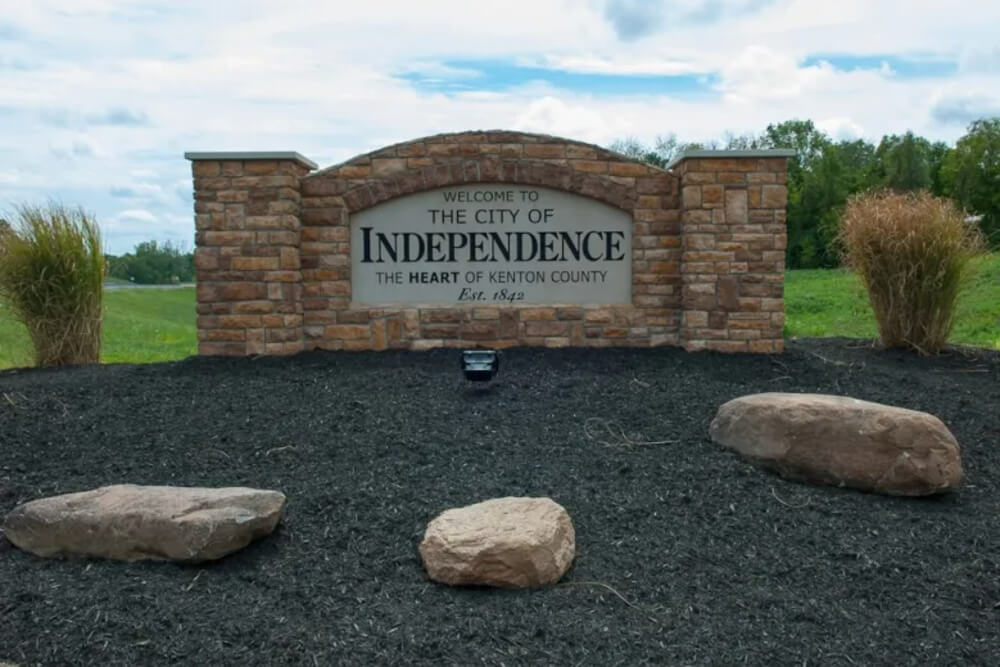 Stone entrance sign: 'Welcome to the City of Independence, The Heart of Kenton County, Est. 1842' with brick pillars and surrounding landscaping rocks.