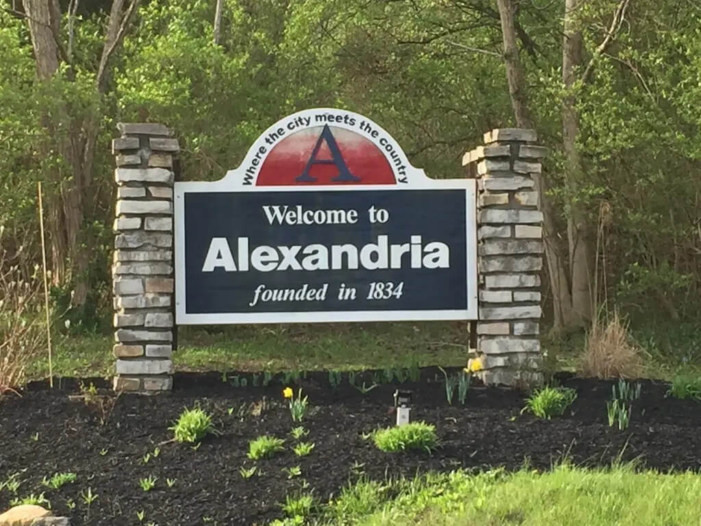 Welcome to Alexandria sign with stone pillars and greenery, noting it was founded in 1834.